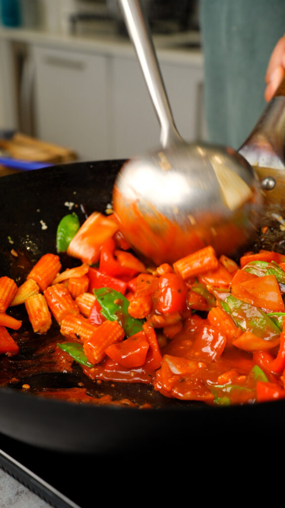 tossing hot and sour sauce with vegetables in a wok