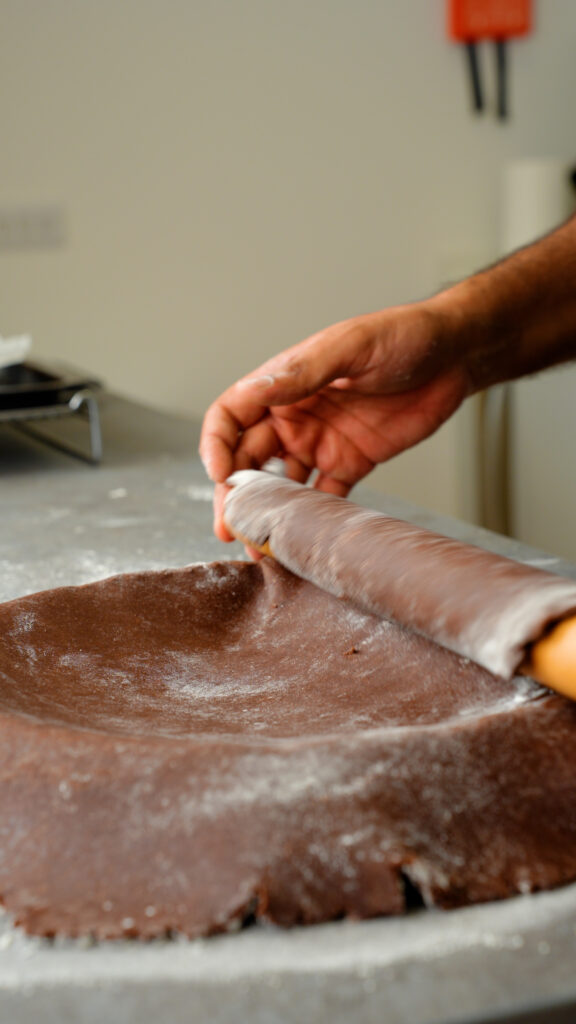 rolling chocolate pastry dough over tart tin