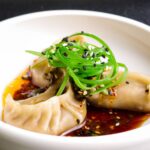 steamed veggie dumplings in a bowl with spring onions on top