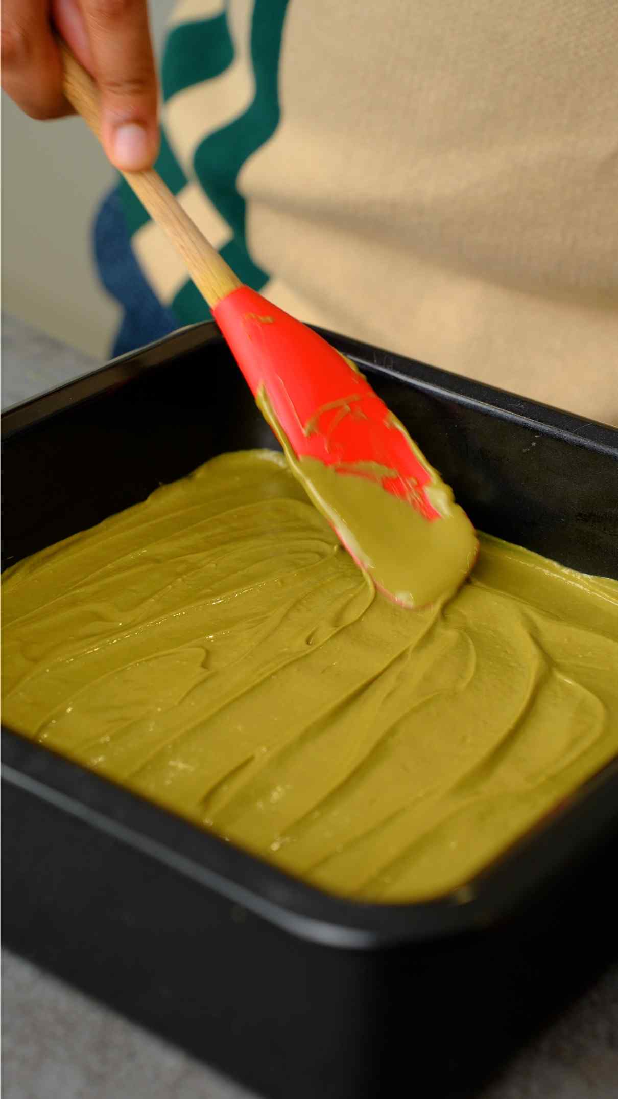 spreading pistachio paste over barfi