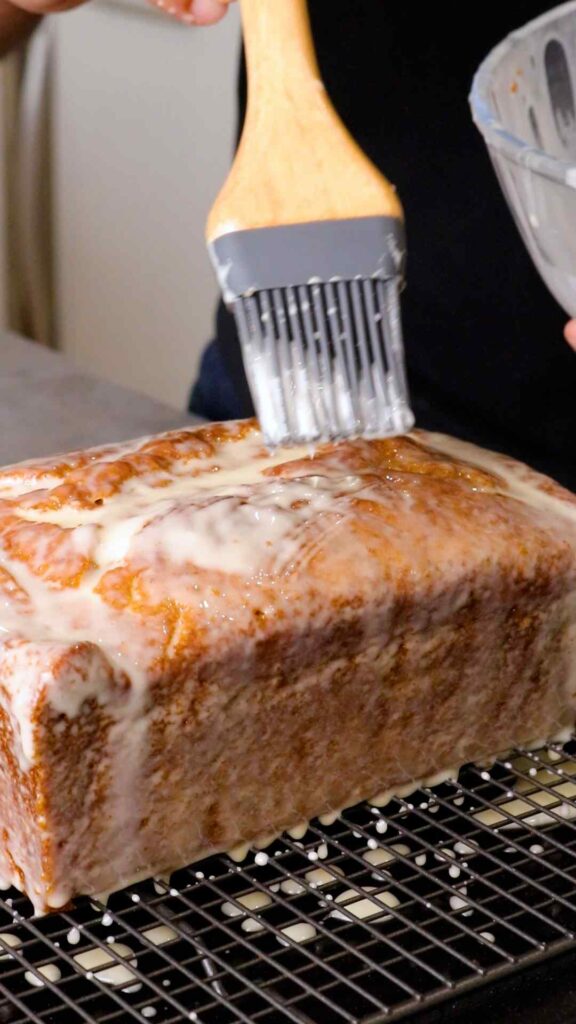 orange glaze being brushed over the orange and pistachio loaf
