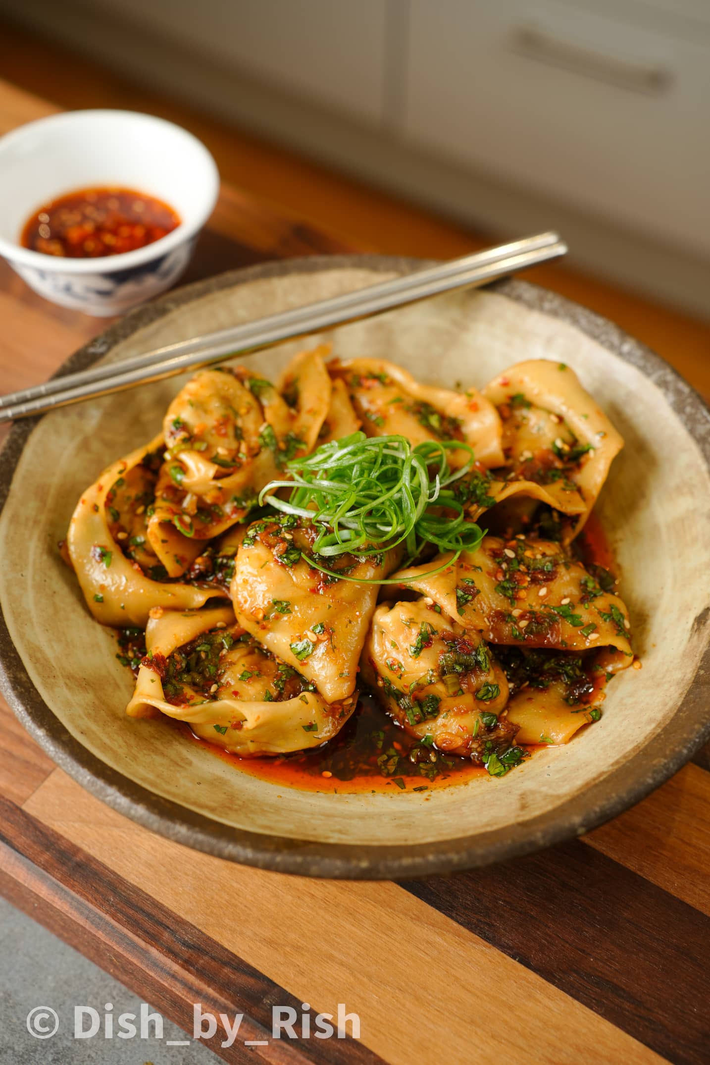 tofu and vegetable wontons in a bowl with chopsticks on top and a bowl of chilli oil next to it