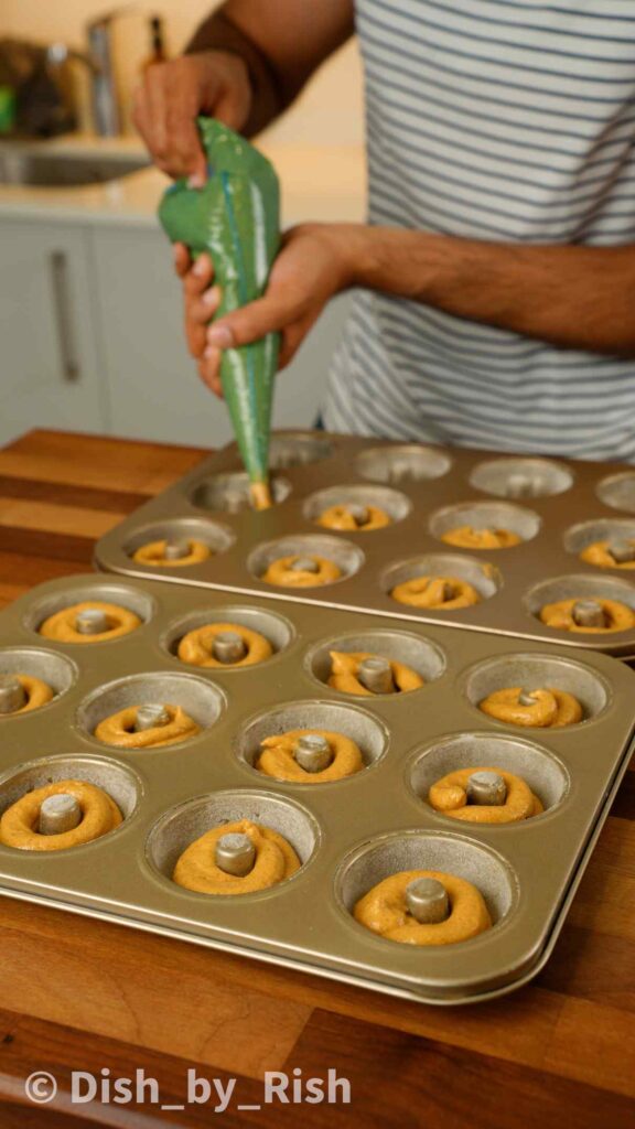 piping pumpkin doughnut batter into doughnut tray