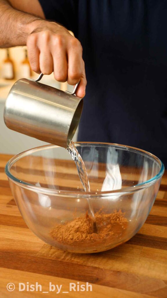 pouring hot water over cocoa powder in a mixing bowl