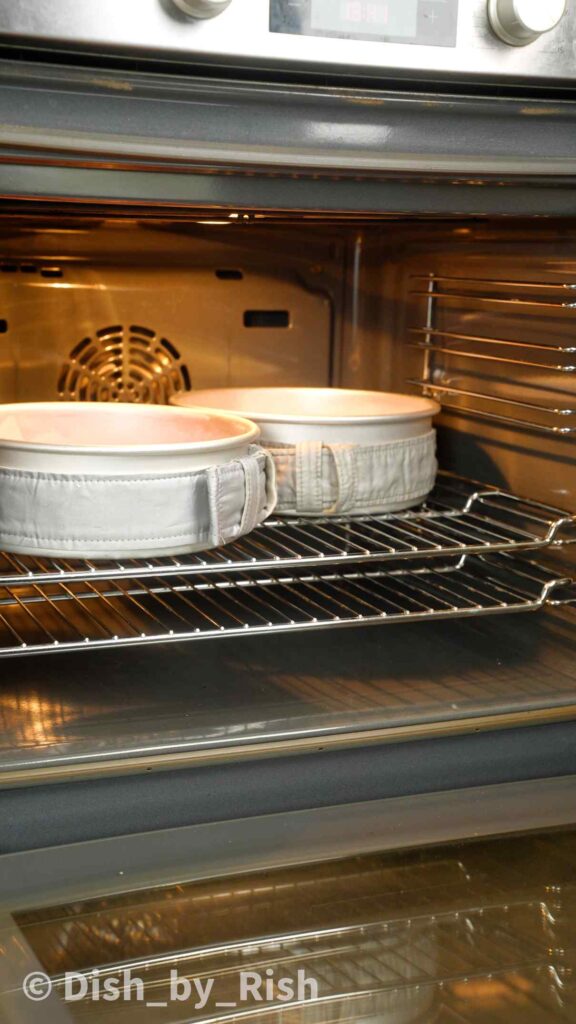 placing cake tins surrounded in cake strips in the oven