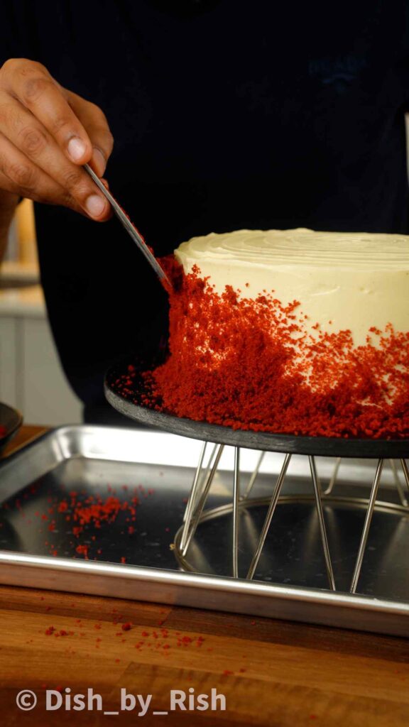 finishing the sides of the red velvet cake with cake crumbs