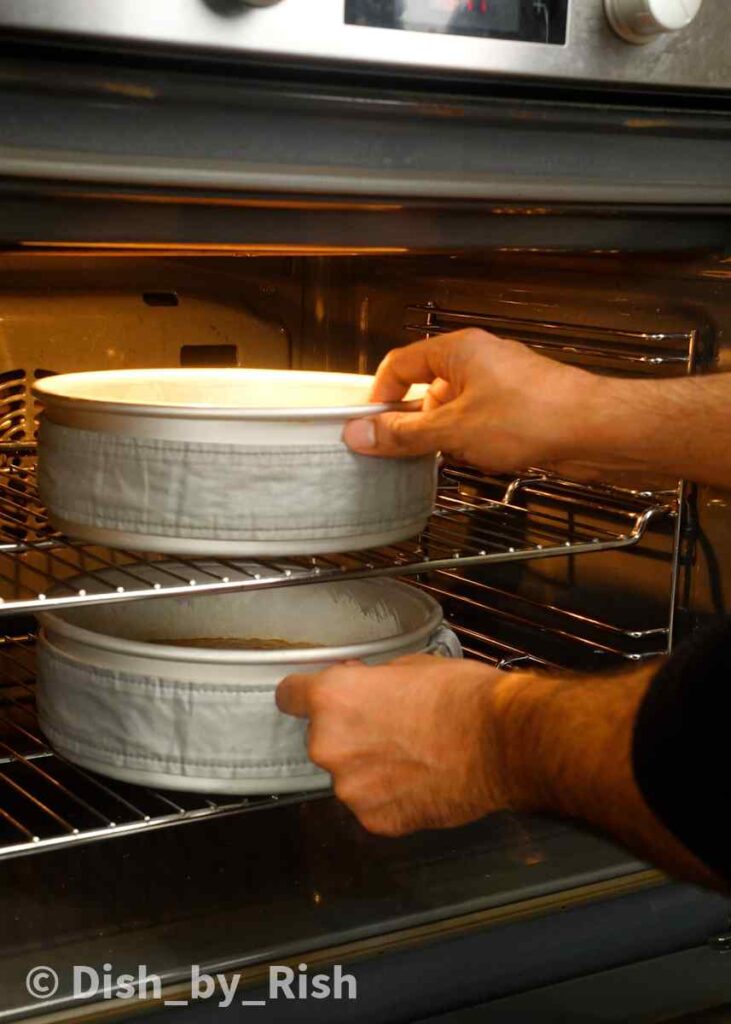 placing carrot cake into the oven with cake strips around the tins