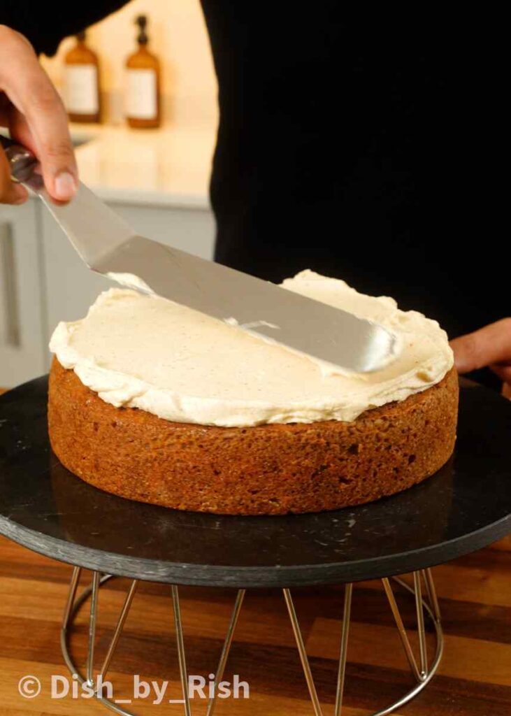 spreading brown butter cream cheese frosting over carrot cake layer