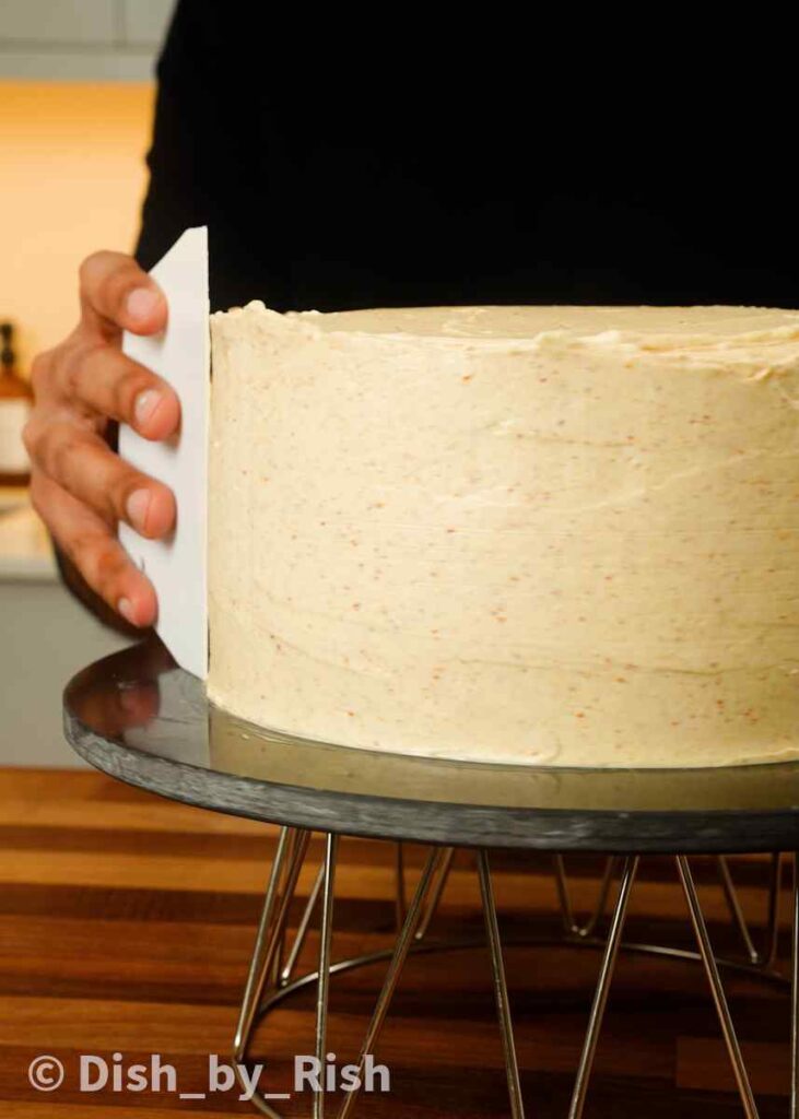 spreading frosting over the sides of the carrot cake