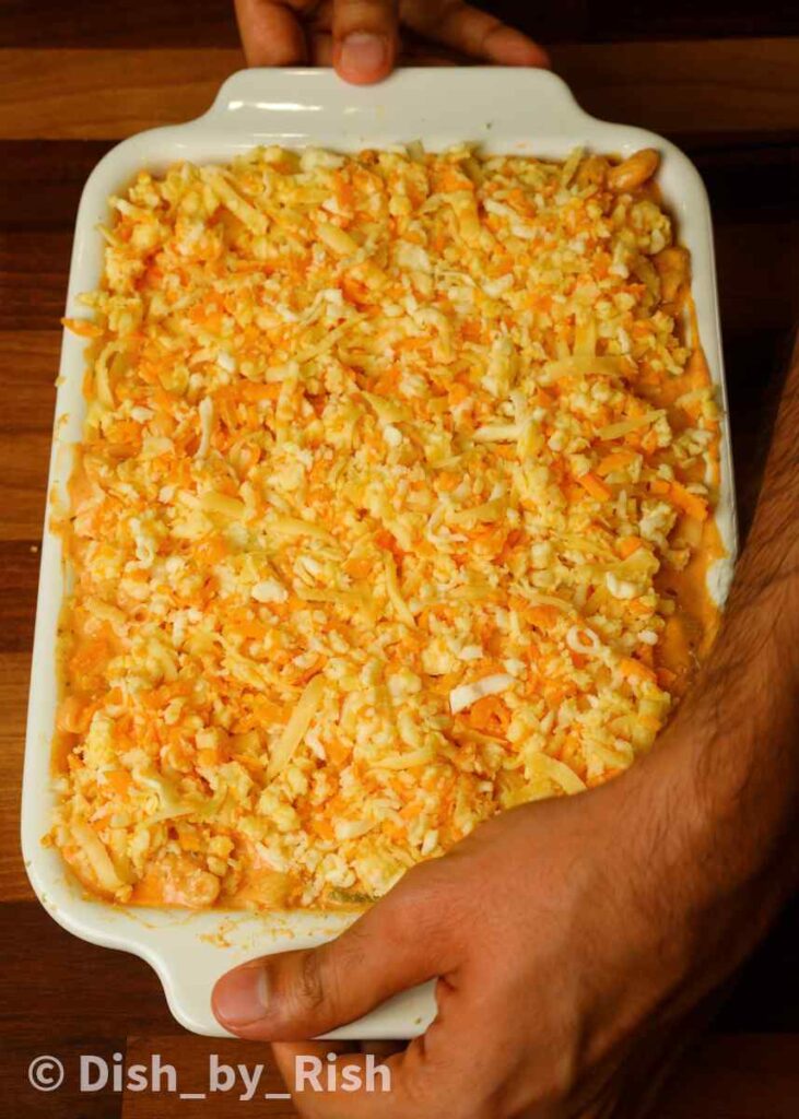 covering mac and cheese in tray with grated cheese