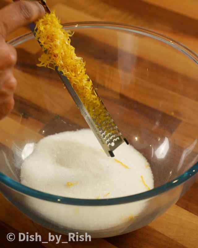 grated lemon zest being added to a bowl of sugar