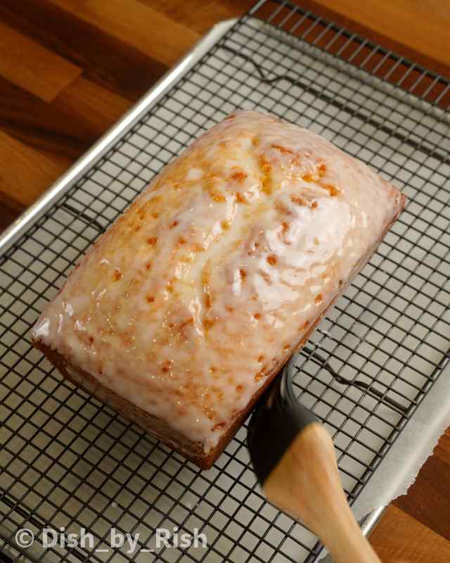 lemon glaze being brushed onto lemon loaf on top of a wire rack