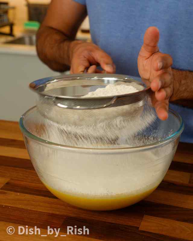 dry ingredients being sifted on top of wet mix in a mixing bowl